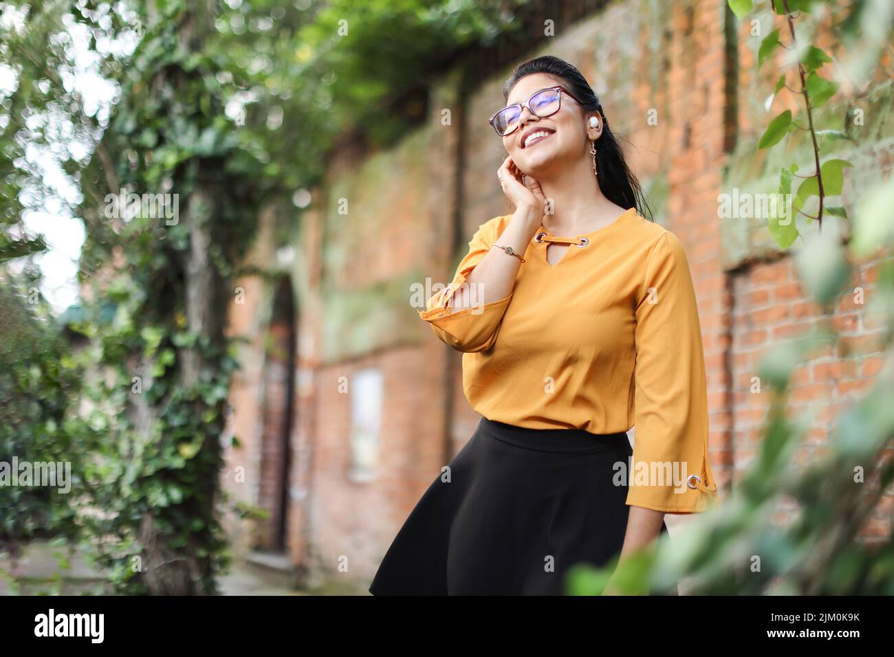 Junge lateinamerikanische Frau mit Brille und Ohrstöpseln, die lächelnd mit Blättern aufschaut, um Platz für Kopien zu schaffen Stockfoto