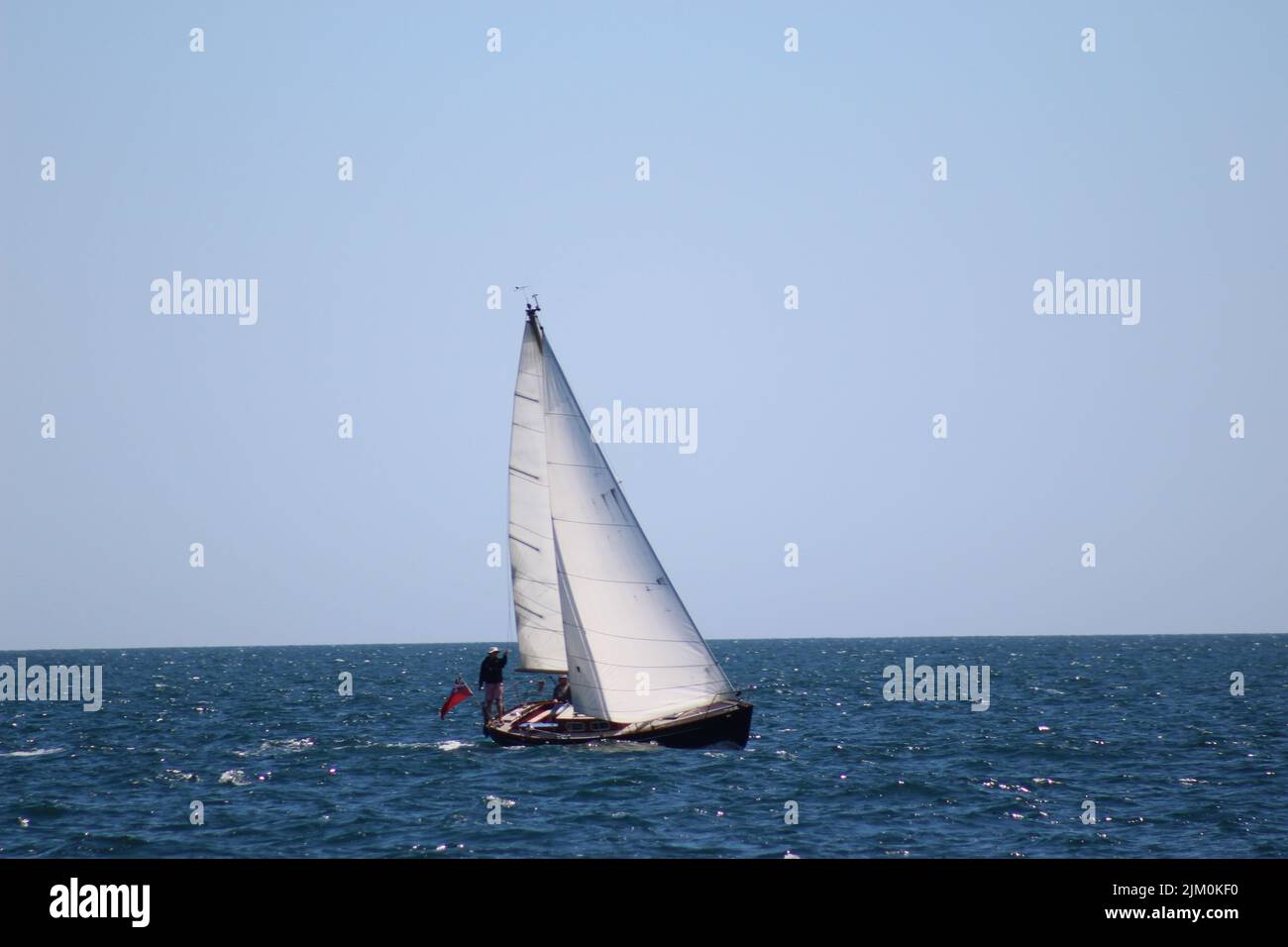 Ein Blick auf Männer, die auf einem schwimmenden Segelboot im Meer unter blauem, hellem Himmel stehen Stockfoto