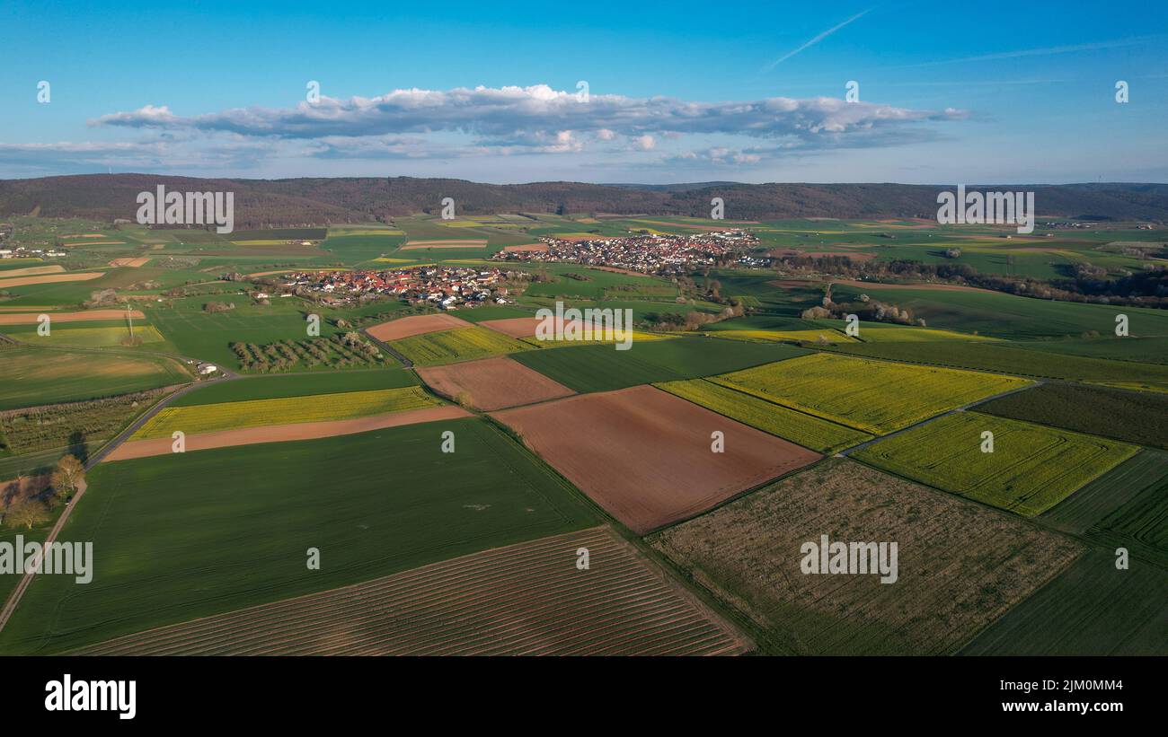 Ein Blick aus der Vogelperspektive auf landwirtschaftliche Felder vor grünen Hügeln an einem sonnigen Tag in Bayern, Deutschland Stockfoto