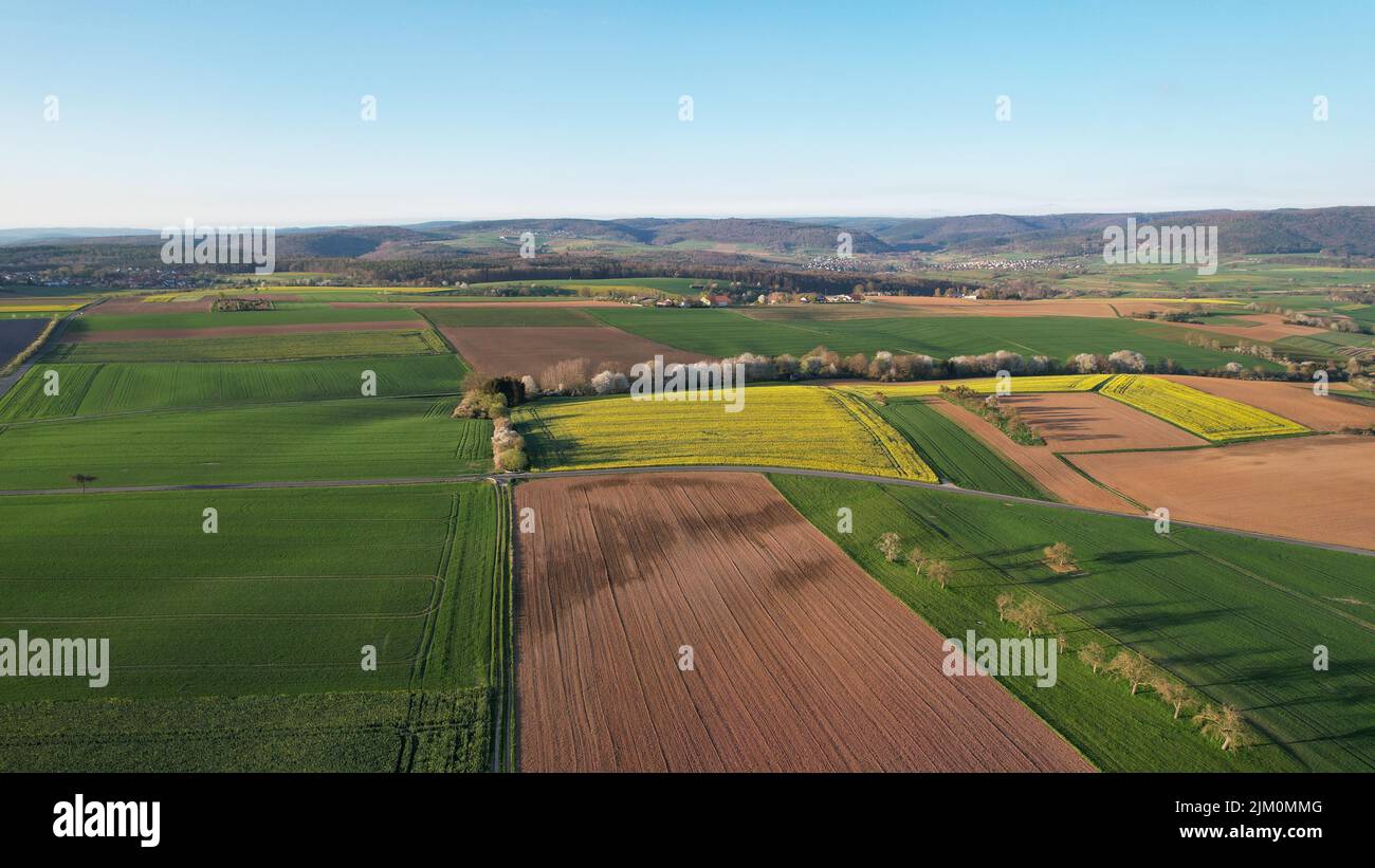 Ein Blick aus der Vogelperspektive auf landwirtschaftliche Felder vor grünen Hügeln an einem sonnigen Tag in Bayern, Deutschland Stockfoto