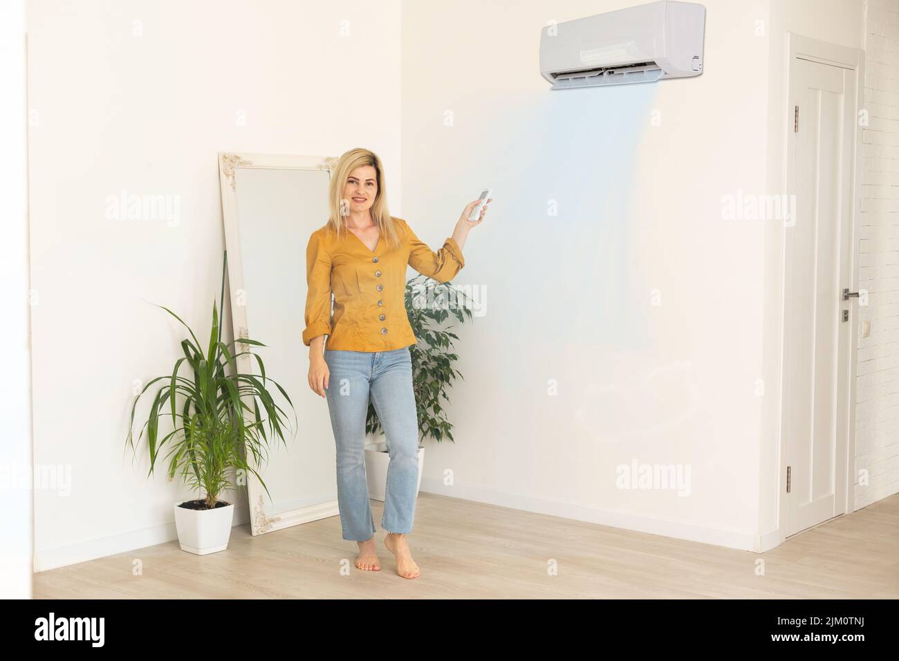 Frau mit Fernbedienung, die auf die Klimaanlage gerichtet ist Stockfoto
