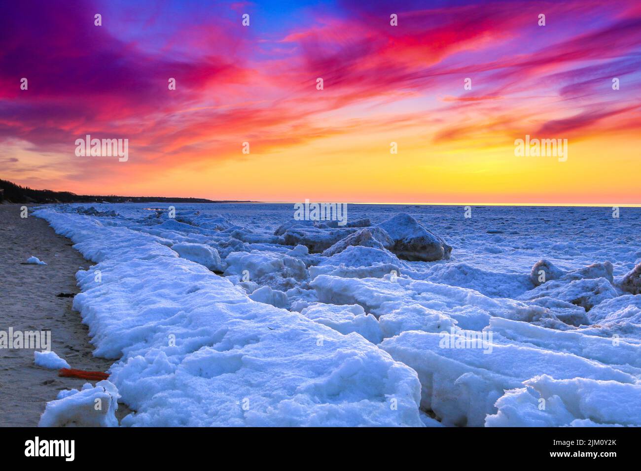 Ein schöner Blick auf eine schneebedeckte Küste bei einem bunten Sonnenuntergang Stockfoto