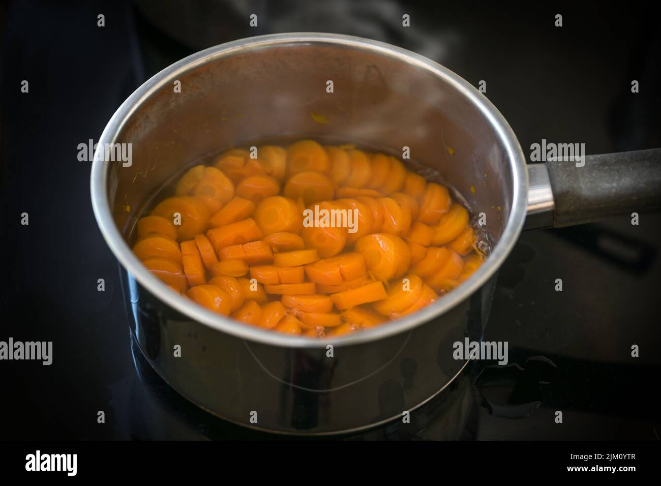 Karottenscheiben werden in Wasser in einem Stahltopf auf einem schwarzen Herd für eine gesunde, verdauliche Gemüsemahlzeit oder Suppe gegen Durchfall gekocht, ausgewählter Brennpunkt, Stockfoto