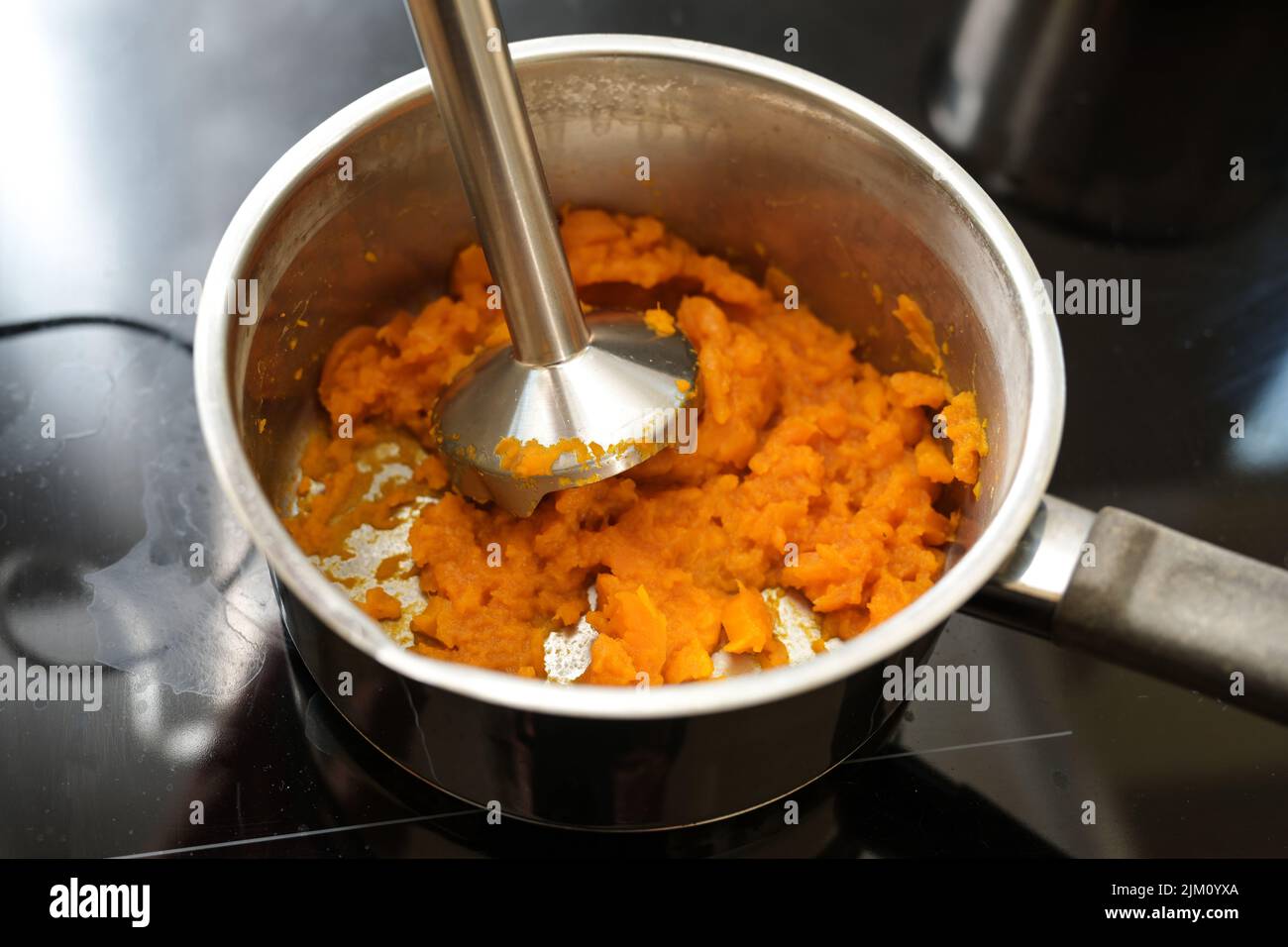 Gekochte Karotten werden mit einem Mixer in einem Stahltopf auf einem schwarzen Herd für ein gesundes, verdauliches Gemüsegericht oder eine Suppe gegen Durchfall, ausgewählt, püriert Stockfoto