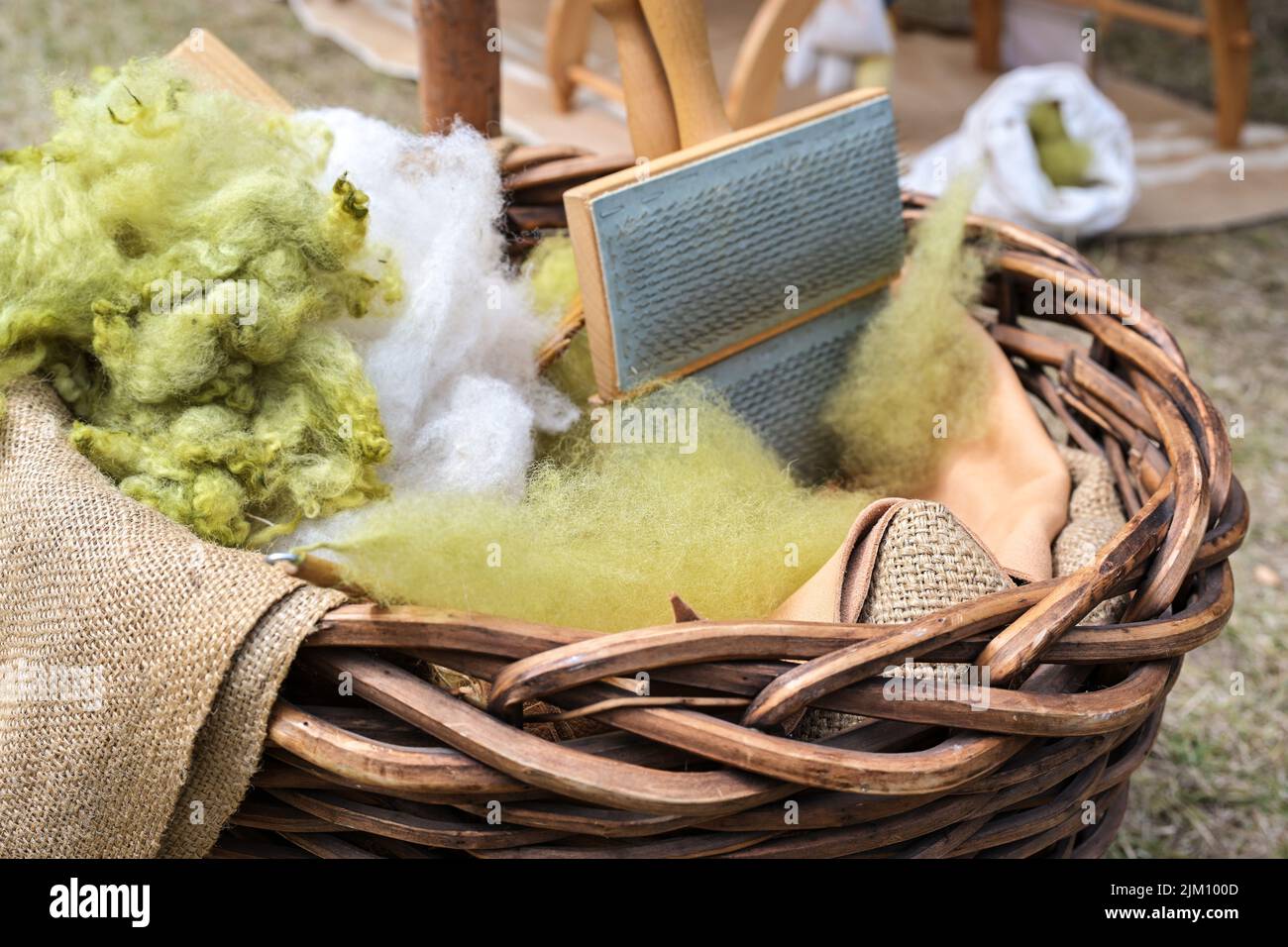 Weiße und grüne Wolle, ungepflegt und mit einer Handkarte in einem Korb brüllt, Vorbereitung zum Spinnen, ausgewählter Fokus, enge Schärfentiefe Stockfoto