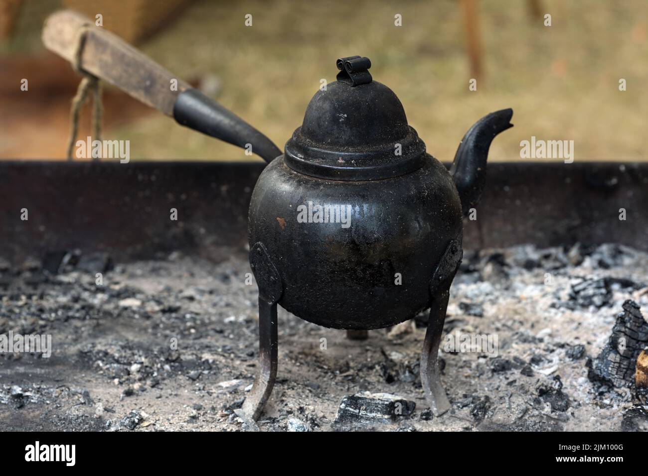 Kleiner Eisenkessel auf drei Beinen mit Holzgriff zum Kochen von Kaffee oder Tee auf offenem Feuer oder Holzkohle, Kopierraum, ausgewählter Fokus, narr Stockfoto