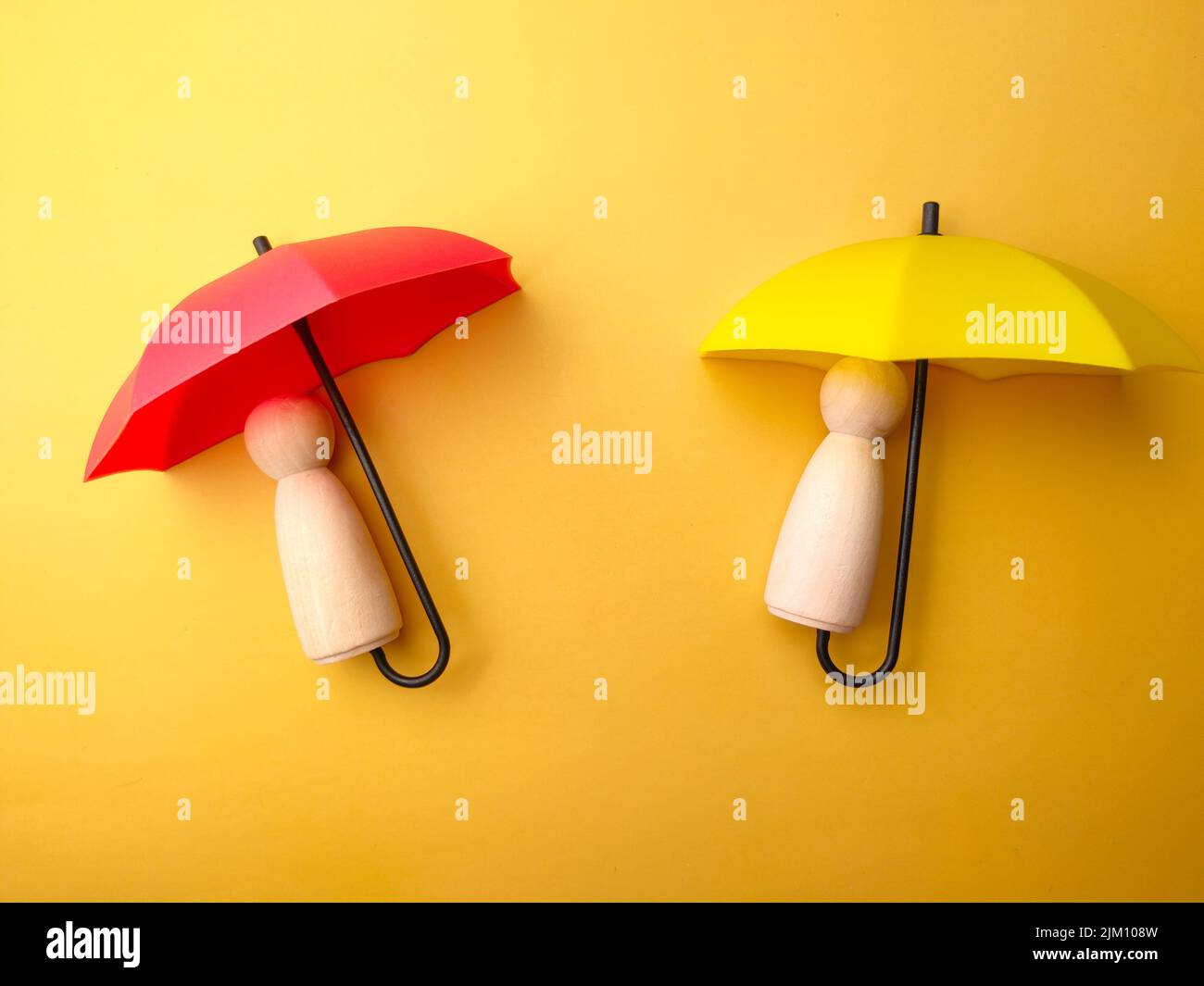 Holzfiguren mit Regenschirm auf gelbem Hintergrund. Persönliches Versicherungskonzept. Stockfoto