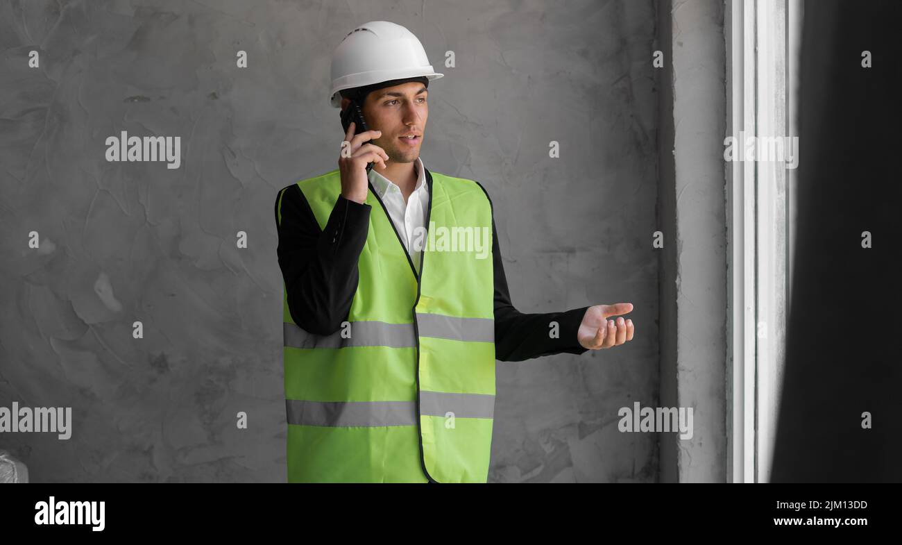 Professioneller junger Baumeister mit Schutzhelm, Telefonanruf, Hausrenovierung und Kommunikation Stockfoto