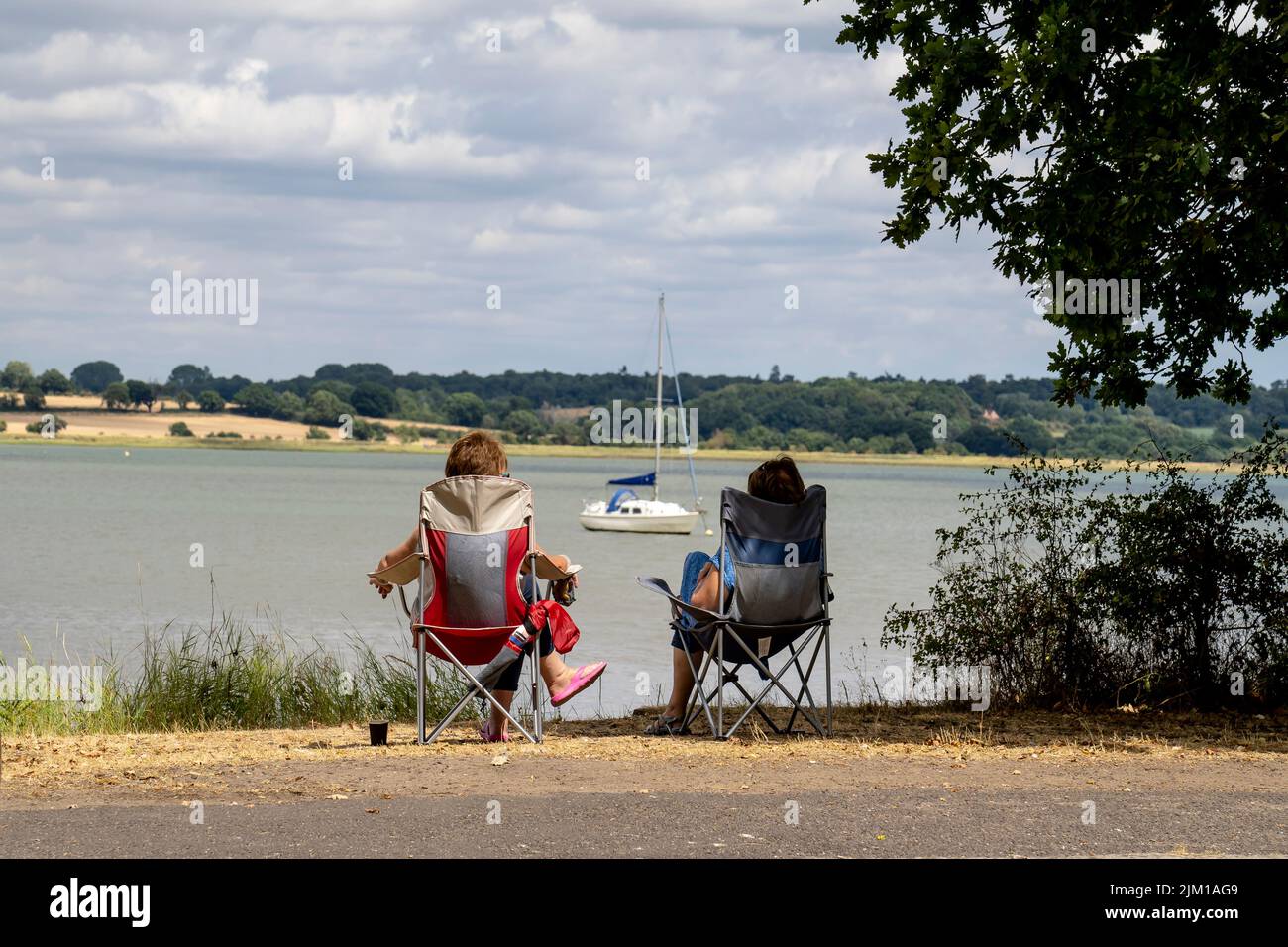 Zwei Damen, die sich auf Stühlen ausruhen und den Blick über den Fluss Stour in Mistley bewundern Stockfoto
