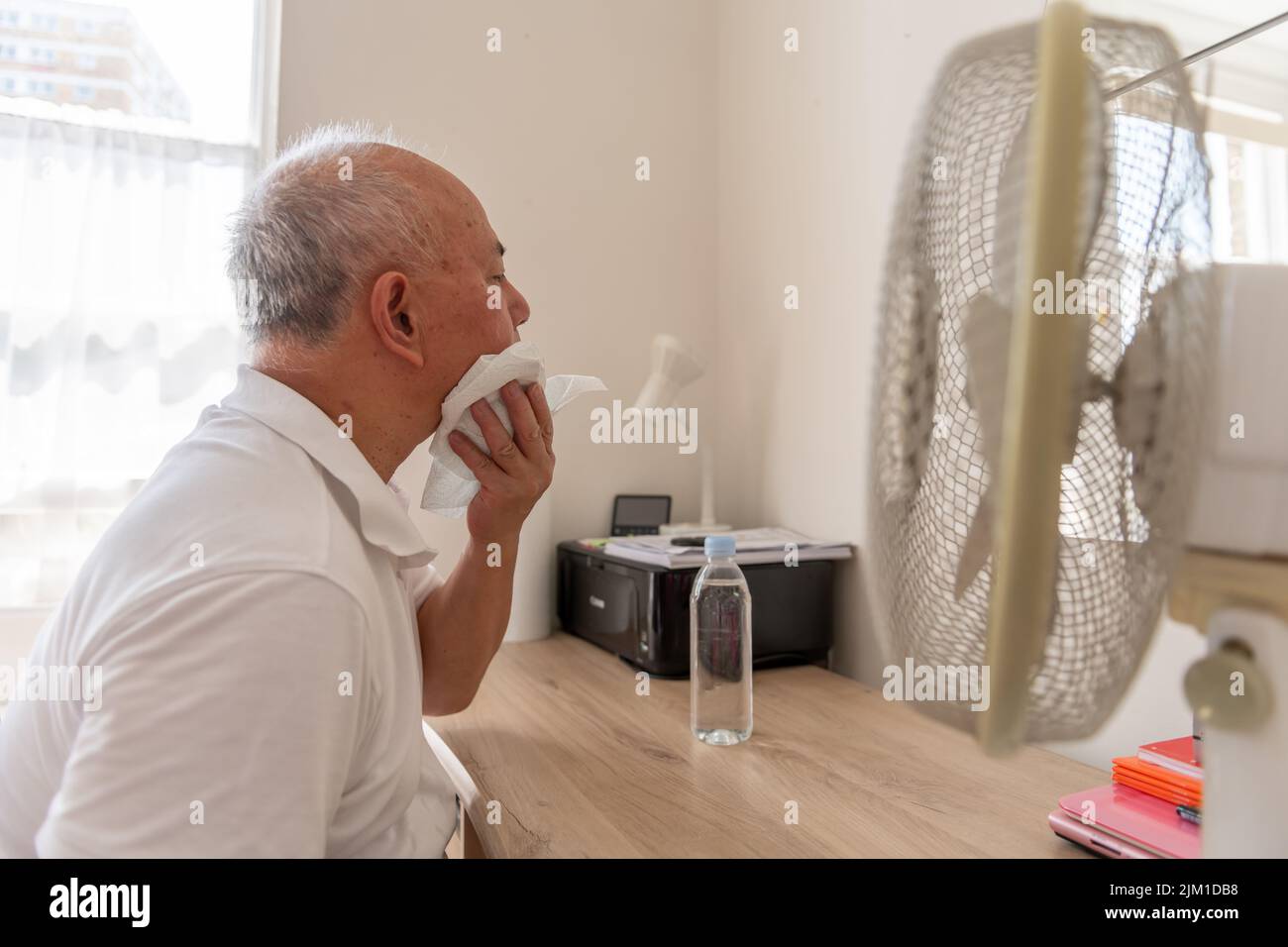 Ein älterer Mann, der unter extrem heißer, rekordbrechender Sommerhitze leidet und versucht, sich zu Hause kühl und gut zu halten. Stockfoto