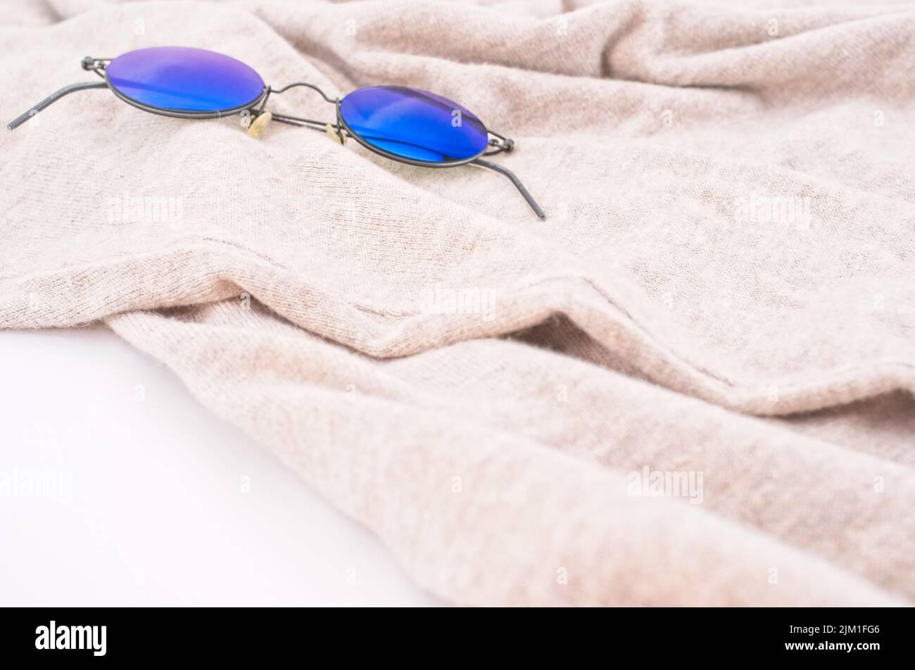 Sonnenbrillen auf einem beigen Wollpullover mit weißem Hintergrund - Lifestyle-Konzept Stockfoto