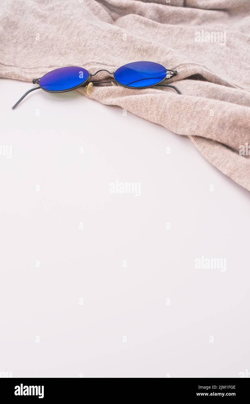 Sonnenbrillen auf einem beigen Wollpullover mit weißem Hintergrund - Lifestyle-Konzept Stockfoto