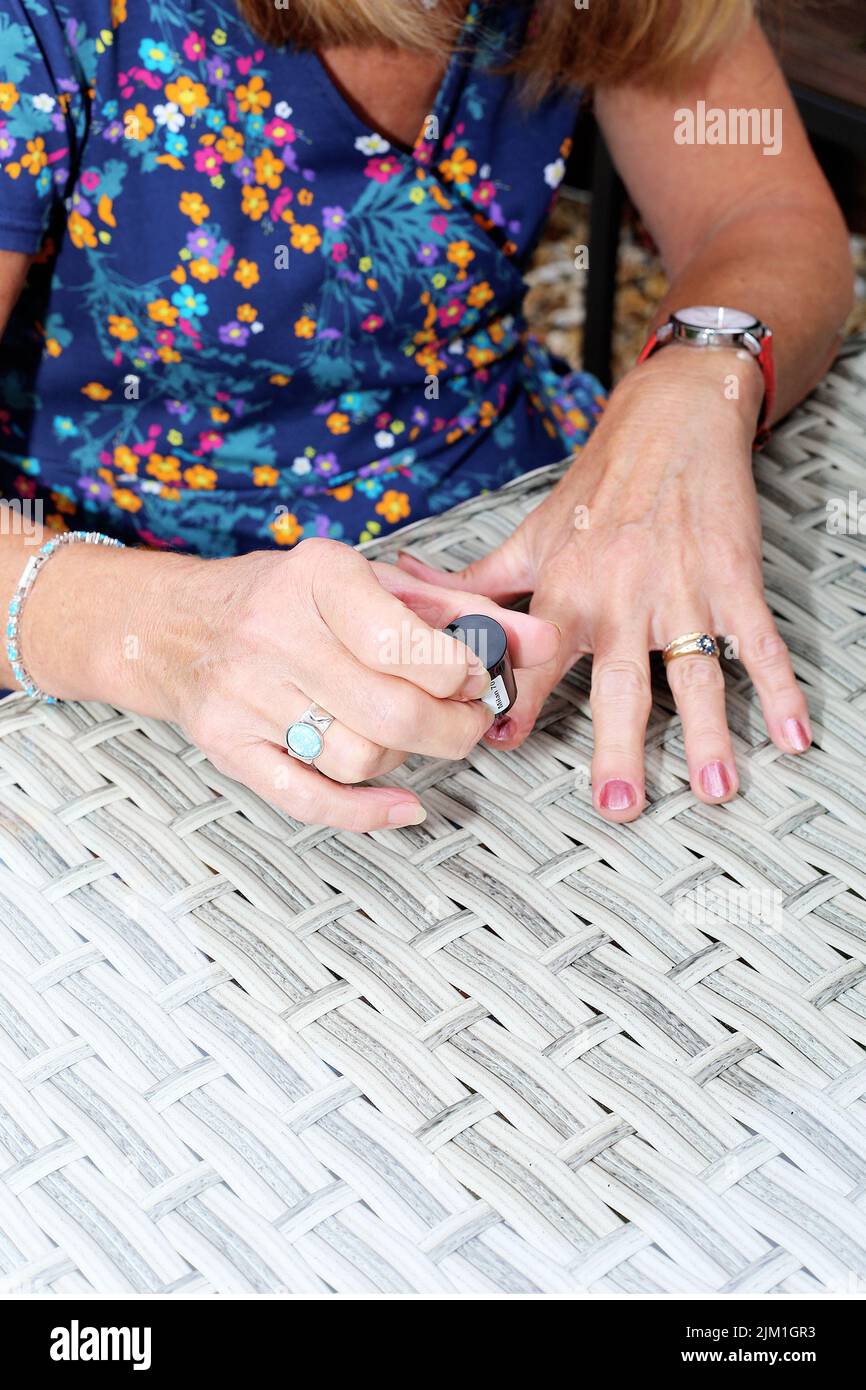 Eine junge Frau trägt Nagellack auf ihre Fingernägel auf einem Gartentisch auf. Stockfoto