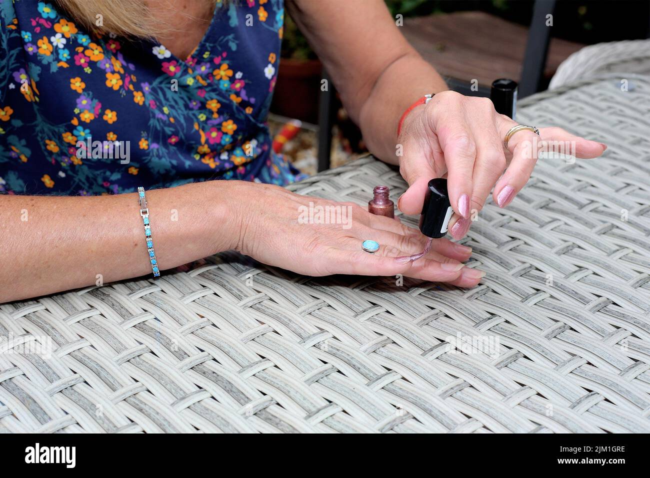 Eine junge Frau trägt Nagellack auf ihre Fingernägel auf einem Gartentisch auf. Stockfoto