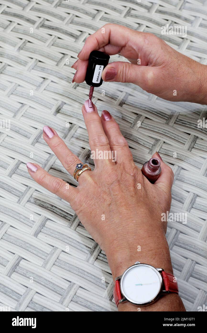 Eine junge Frau trägt Nagellack auf ihre Fingernägel auf einem Gartentisch auf. Stockfoto