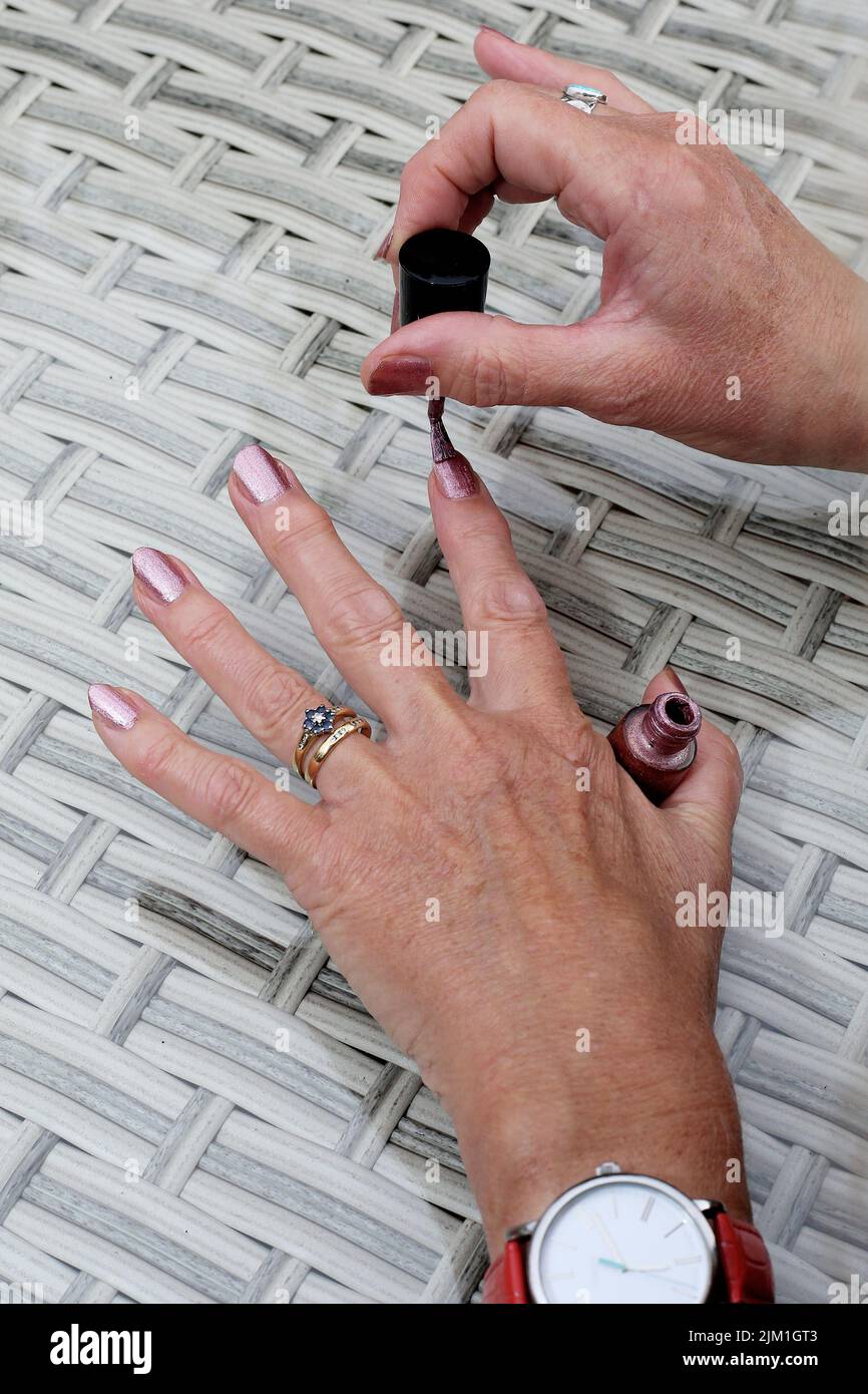 Eine junge Frau trägt Nagellack auf ihre Fingernägel auf einem Gartentisch auf. Stockfoto
