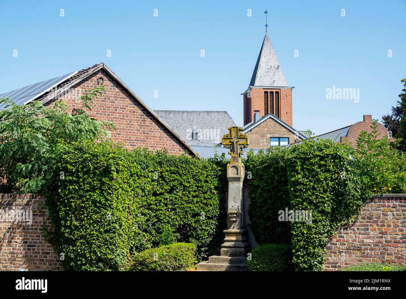 Deutschland, NRW, Kreis Düren, Vettweiß, Wegekreuz au18. Jh.am Marktplatz, hinter der Turm der katholischen Pfarrkirche Sankt Gereon Stockfoto