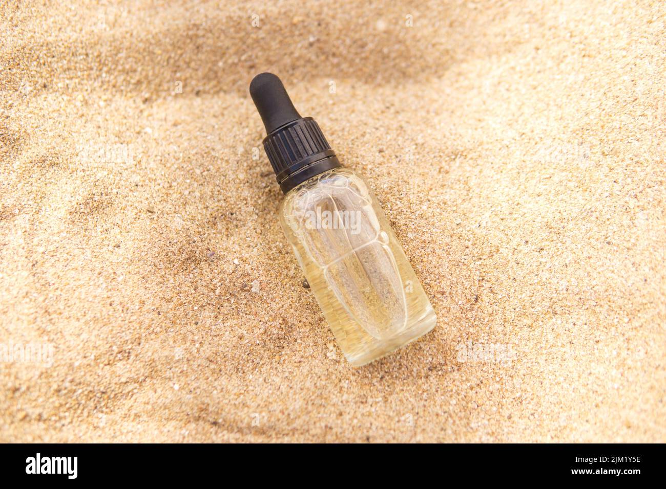 Kosmetisches Serum in einer Glasflasche mit einer Pipette im Sand Stockfoto