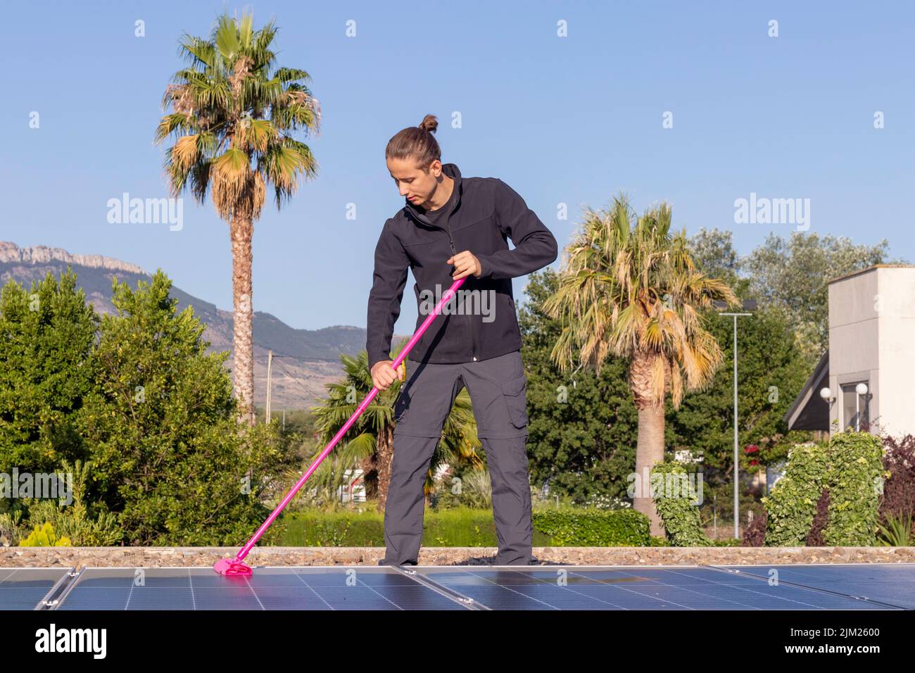 Seitenansicht eines jungen Mannes, der die Sonnenkollektoren eines Solarkraftwerks für erneuerbare und saubere Energie reinigt Stockfoto