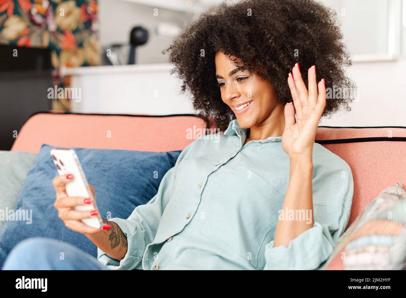 Glückliche afroamerikanische Frau, die die mobile App auf dem Smartphone nutzt, um einen Videoanruf zu tätigen, die Hand zu winken und Freunde oder Familie zu grüßen, über eine Videoverbindung zu sprechen und auf Distanz in Kontakt zu bleiben Stockfoto