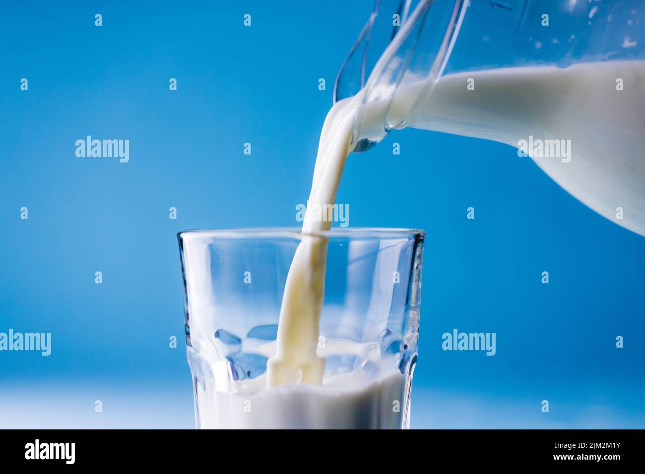 Nahaufnahme der Milch, die aus dem Glas auf blauem Hintergrund in das Glas gegossen wird, Platz kopieren Stockfoto