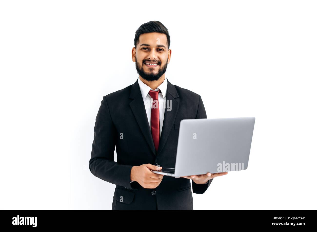 Positiv elegant attraktiver indischer oder arabischer Mann im Business-Anzug, Unternehmer, der einen offenen Laptop in den Händen hält, die Kamera anschaut, auf einem isolierten weißen Hintergrund steht und freundlich lächelt. Kopierbereich Stockfoto
