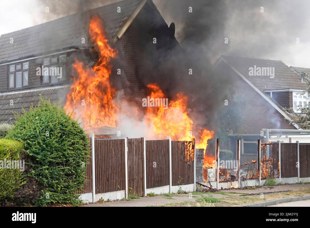 Flammen von verschiedenen Haushaltsgegenständen, die im Freien neben dem Holzgrenzzaun gelagert wurden, entzündeten sich bei der sengenden Sommerhitze und entzündeten sich so gegen die Hauswand in Großbritannien Stockfoto