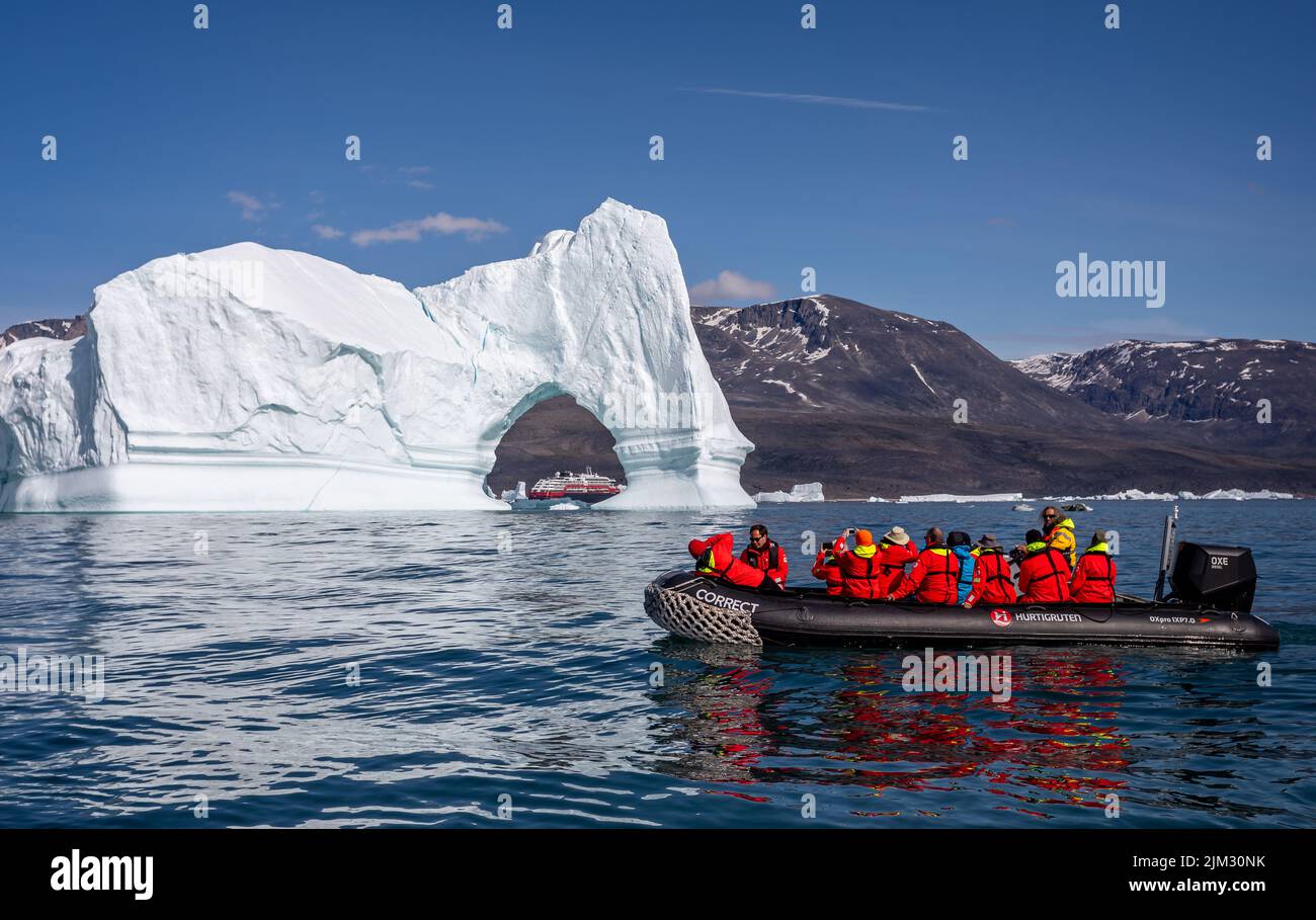 Hurtigrutes Expeditionskreuzfahrtschiff MS Fridtjof Nansen, gesehen durch einen Bogen in einem giganten Eisberg mit Tierkreis unerschrockener Touristen im Vordergrund Stockfoto