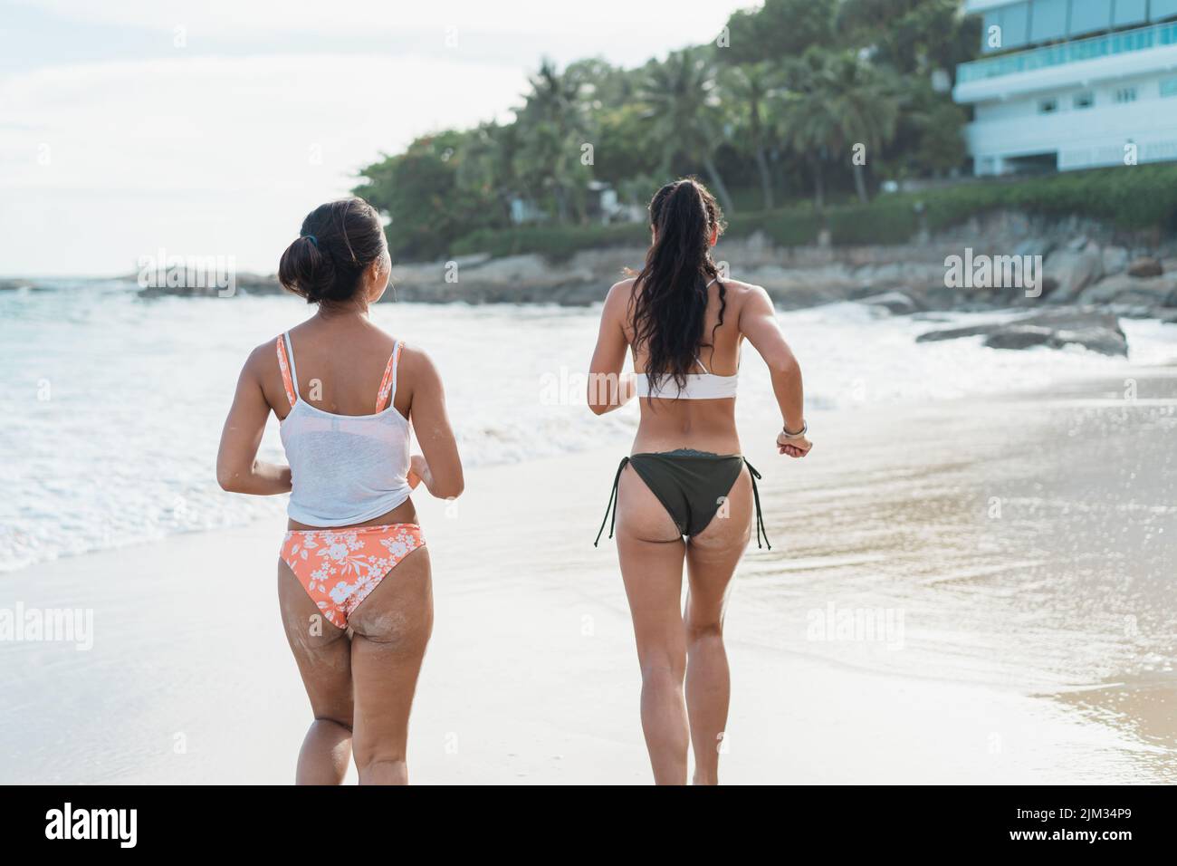 Rückansicht der schönen 2 Frauen im Bikini, die am Strand zum Meer laufen. Hübsche junge asiatische Reisende in Badekleidung, die Spaß haben, während sie am Wochenende tropischen Urlaub genießen Stockfoto