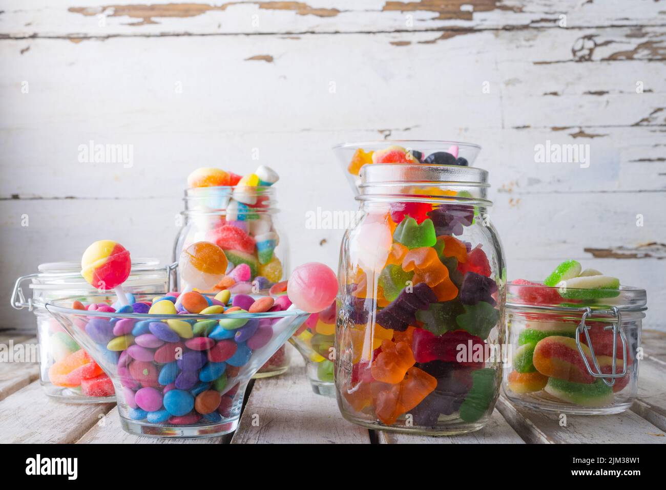 Nahaufnahme von bunten Süßigkeiten und Lutschern in Gläsern und Schüssel auf Holztisch Stockfoto