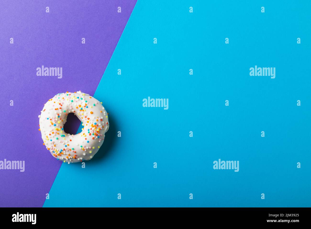 Deckenansicht des frischen weißen Donuts mit Sprinklern durch einen Kopierraum vor zweifarbigem Hintergrund Stockfoto