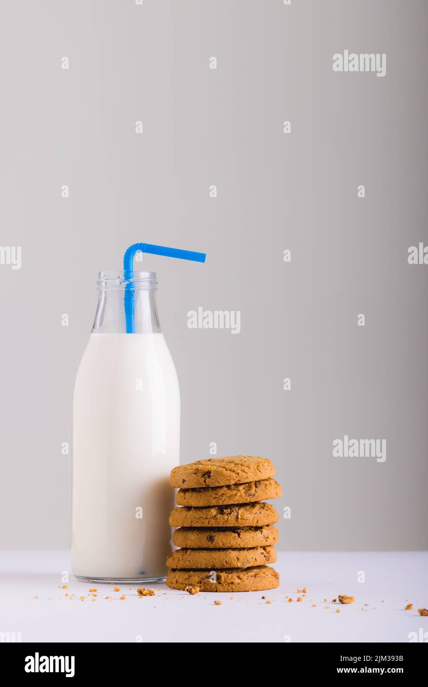 Milchflasche mit Stroh durch Stapel von Cookies vor weißem Hintergrund, Platz kopieren Stockfoto