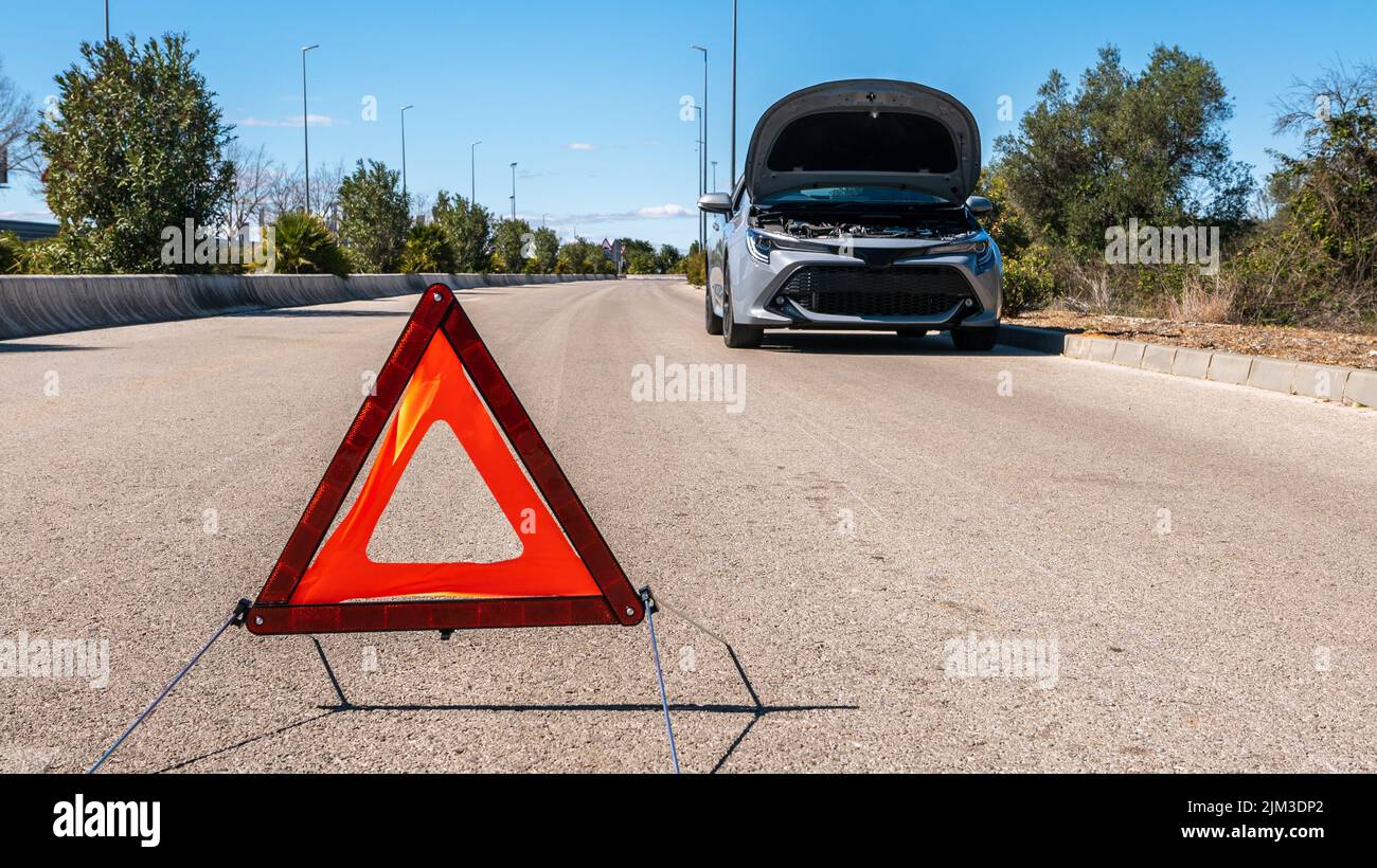Auto mit Problemen und einem roten Dreieck, um andere Verkehrsteilnehmer zu warnen. Ein kaputtes Auto mit offener Haube. Unfall auf der Straße Konzept. Stockfoto