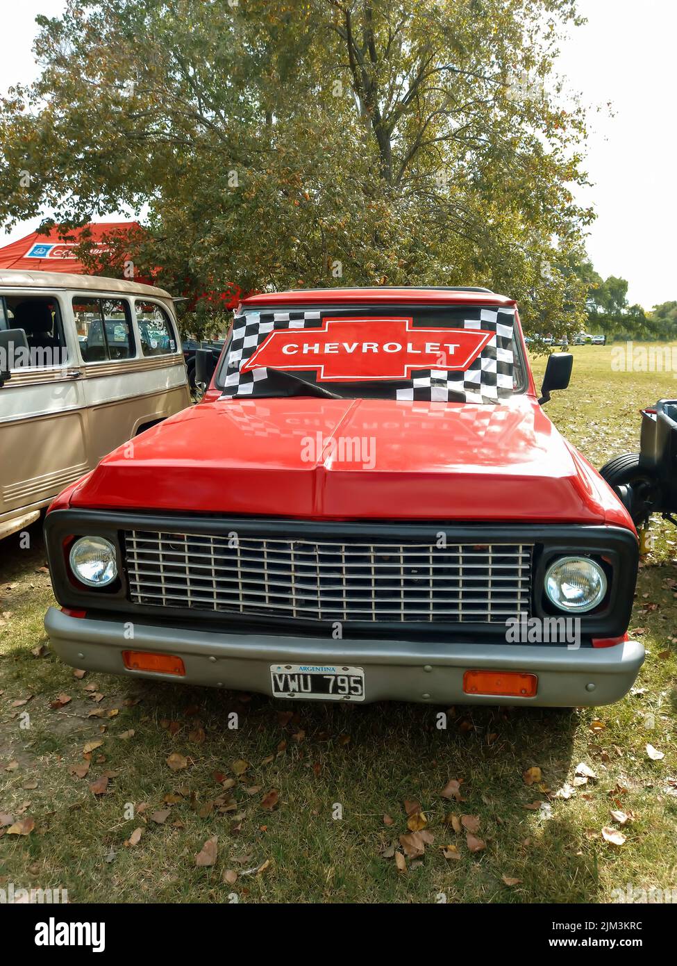 Chevrolet-Emblem auf der Windschutzscheibe eines alten roten Pickup-Trucks aus der Zeit um 1960. Grünes Gras Natur. Vorderansicht. Grill. Oldtimer-Show. Copyspace Stockfoto
