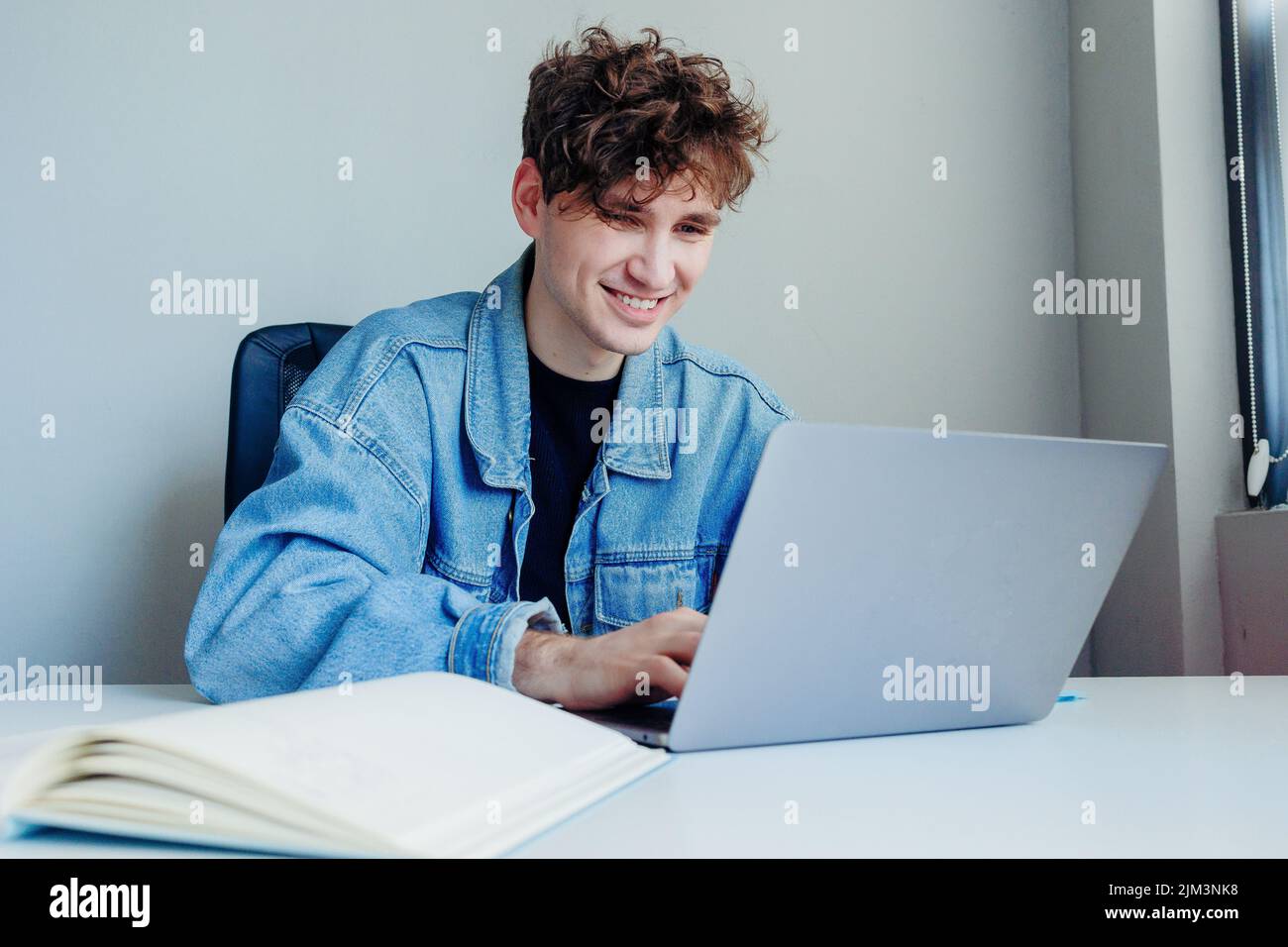 Ein lächelnder junger Mann, der im Büro oder zu Hause an seinem Laptop arbeitet Stockfoto