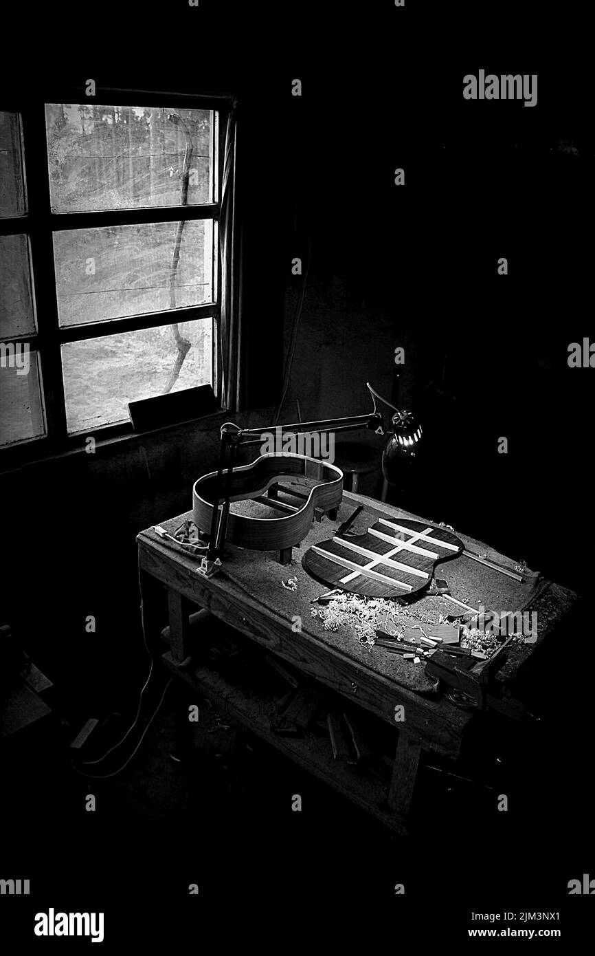 Eine vertikale Aufnahme eines Workshops für dunkle Musik mit Gitarrenparts auf dem Tisch in der Nähe eines offenen Fensters Stockfoto