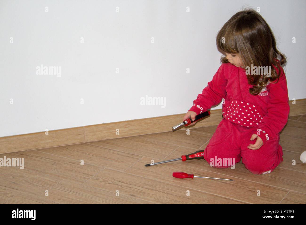 Bild eines entzückenden kleinen Mädchens, das mit dem Werkzeugkasten ihres Vaters in ihrem Schlafzimmer spielt Stockfoto