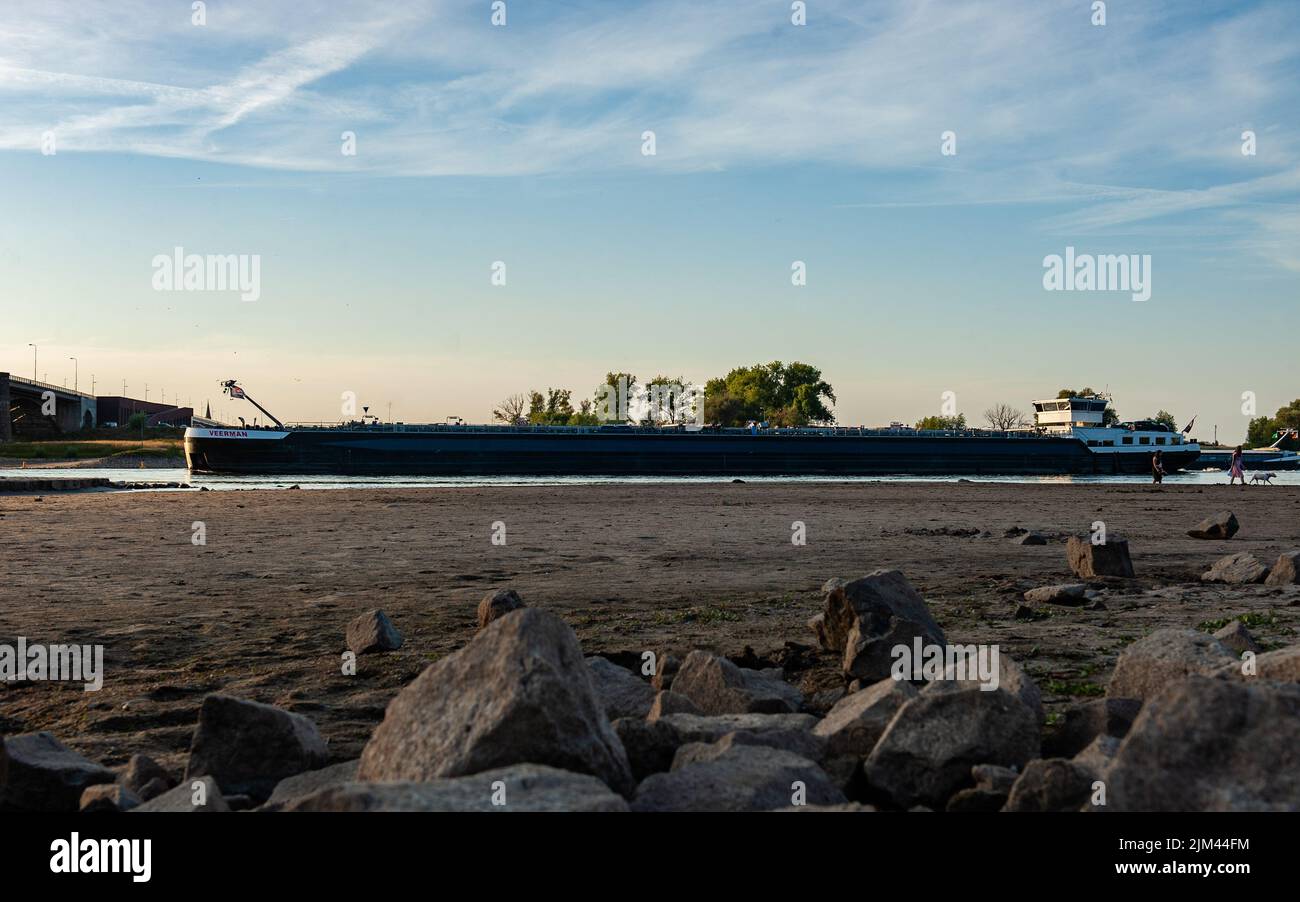 Ein Frachtschiff überquert den Waal-Fluss, auch wenn der Wasserstand niedrig ist. Aufgrund der anhaltenden Dürre leiden die Niederlande offiziell an Wasserknappheit, teilte die Regierung mit. Das knappe Wasser wird gemäß den gesetzlichen Vereinbarungen verteilt, so dass Deiche, Torfböden und sehr gefährdete Naturgebiete so lange wie möglich mit Wasser versorgt werden. Weitere Maßnahmen werden in den kommenden Wochen folgen. Da zwei Drittel der niederländischen Bevölkerung unter dem Meeresspiegel leben, können Dürren in den Niederlanden schnell zu einem akuten Problem werden, was dazu führt, dass Flüsse zum Verstummen kommen und den Wasserverkehr behindern. Aufgrund von t Stockfoto