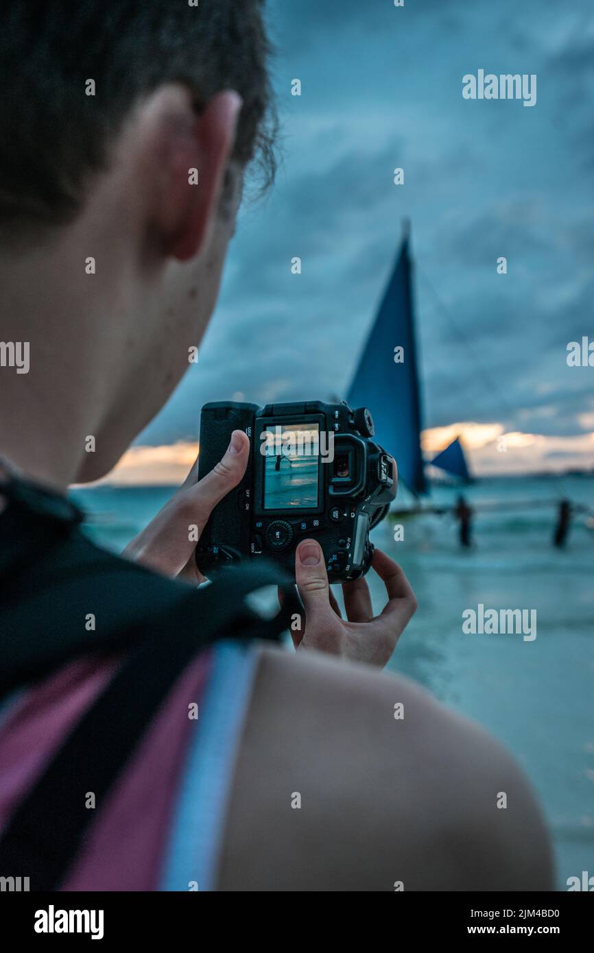 Eine vertikale Aufnahme einer Person, die Bilder von Segelbooten auf dem Wasser in Boracay, Philippinen, macht Stockfoto