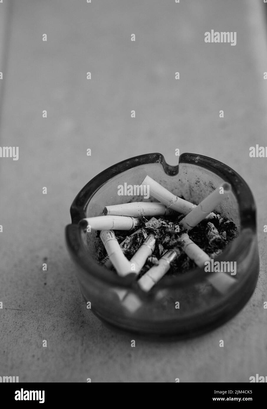 Eine vertikale Nahaufnahme von Zigarettenkippen in einem vollen Aschenbecher in Graustufen mit Copyspace Stockfoto