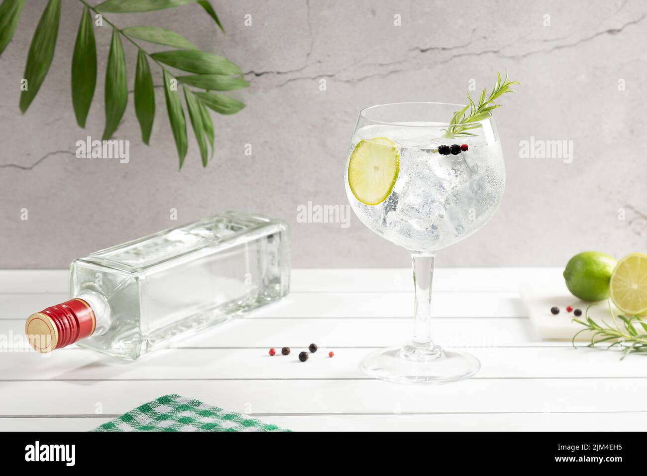 Kaltes Glas Gin Tonic und Flasche auf weißem Holzsockel auf hellem Hintergrund. Stockfoto