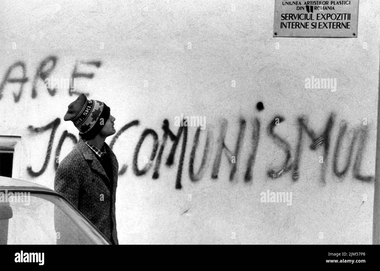 Bukarest, Rumänien, Januar 1990. Tage nach der antikommunistischen Revolution in Rumänien von 1989 kommt ein Mann an einem Gebäude vorbei, in dem jemand „nieder mit dem Kommunismus“ besprüht, eine Handlung, die einen Monat zuvor undenkbar war. Stockfoto