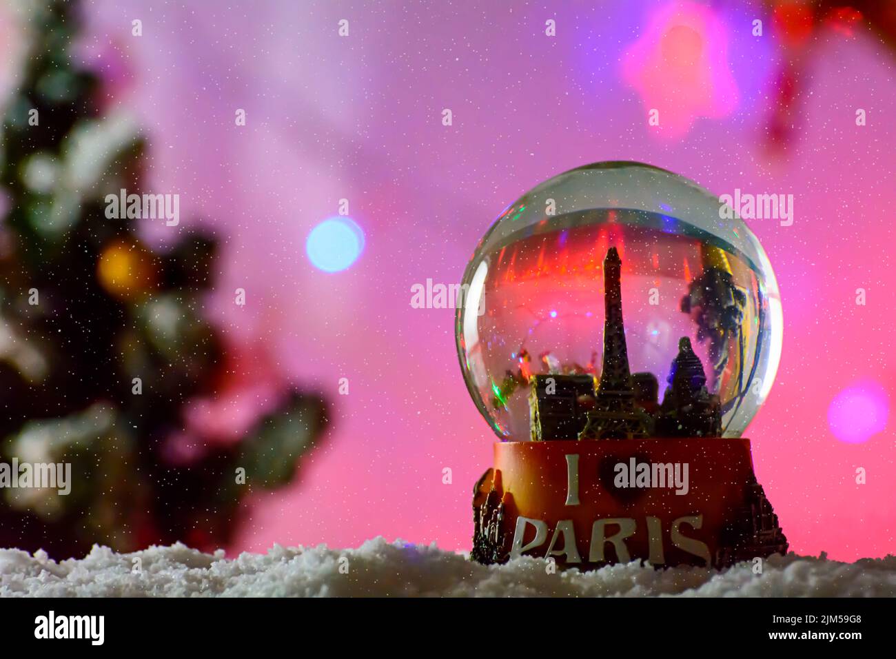 Eine Nahaufnahme schoss ein Schneekugel-Souvenir des Pariser Eiffelturms auf den Schneeflocken auf einem unscharfen violetten Hintergrund Stockfoto