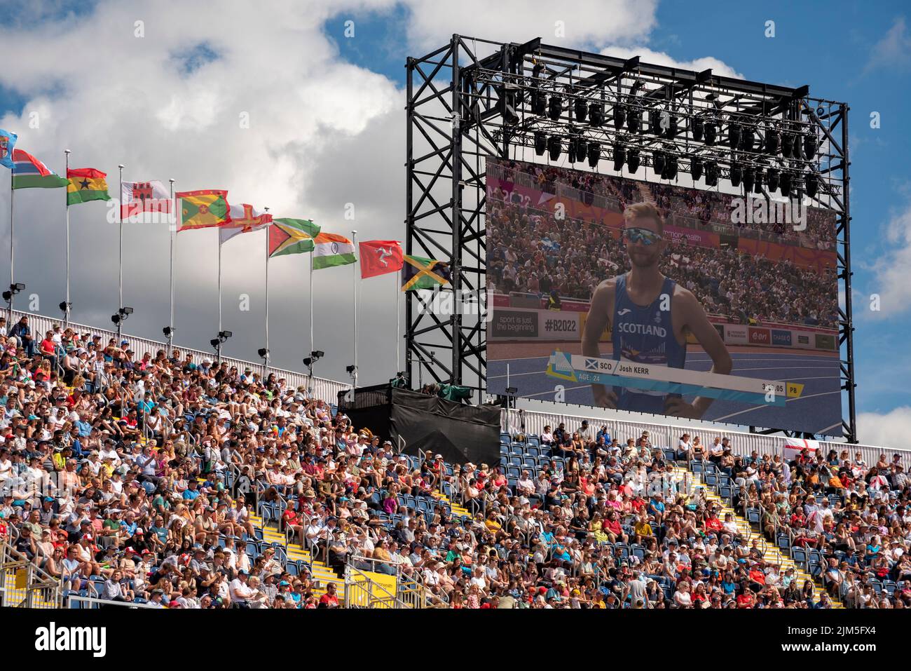 Birmingham, Großbritannien, 4.. August 2022. Zuschauer im Alexander Stadium, Birmingham, genießen die Leichtathletik bei den Commonwealth Games 2022. Flaggen der Commonwealth-Staaten fliegen über das Stadion. Josh Kerr aus Schottland, auf der Leinwand gesehen, qualifizierte sich für die Männer 1500m. Quelle: Martin Anderson/Alamy Live News Stockfoto