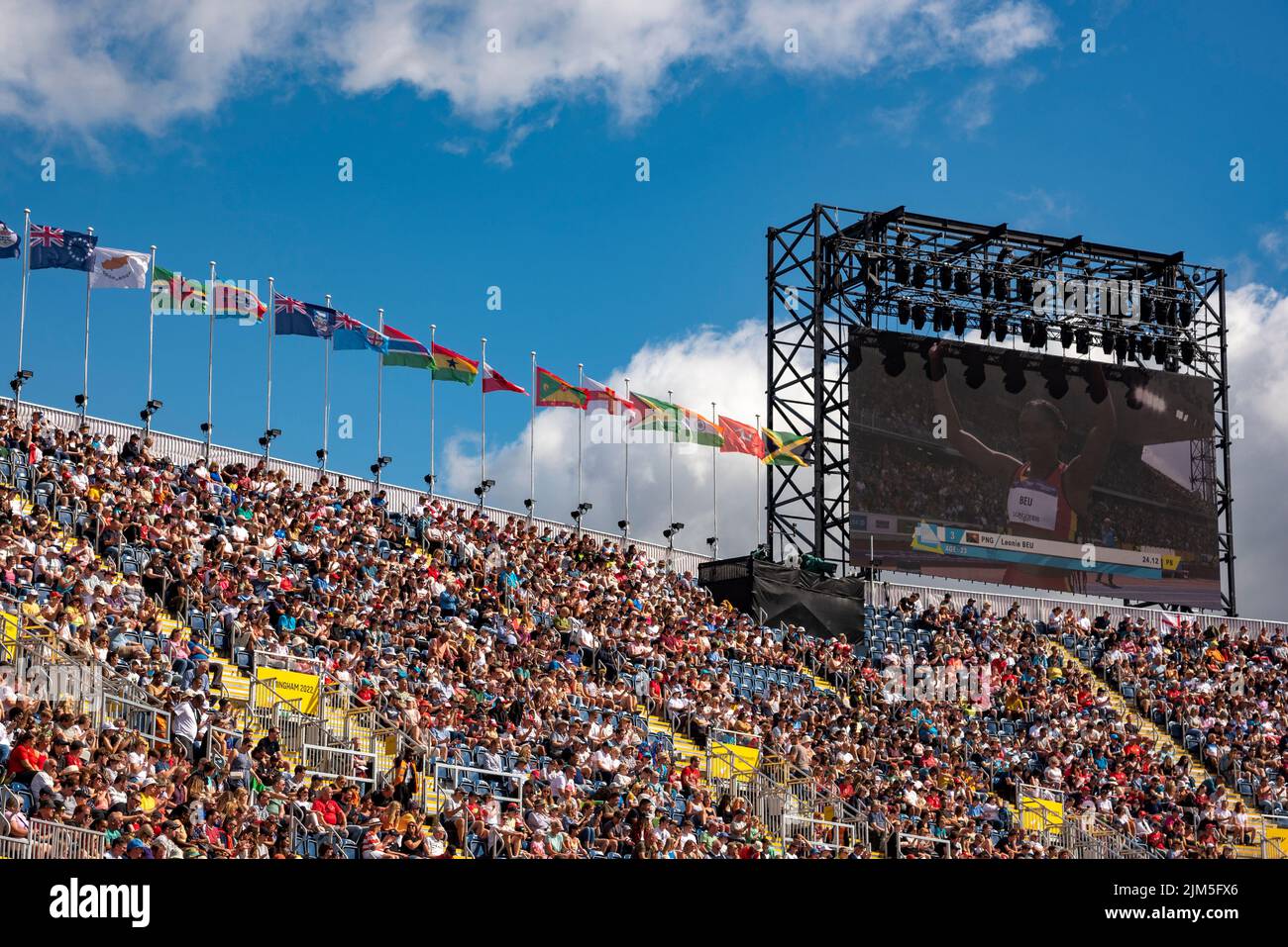 Birmingham, Großbritannien, 4.. August 2022. Zuschauer im Alexander Stadium, Birmingham, genießen die Leichtathletik bei den Commonwealth Games 2022. Flaggen der Commonwealth-Staaten fliegen über das Stadion. Leonie Beuu aus Papua-Neuguinea ist auf dem Bildschirm zu sehen. Quelle: Martin Anderson/Alamy Live News Stockfoto