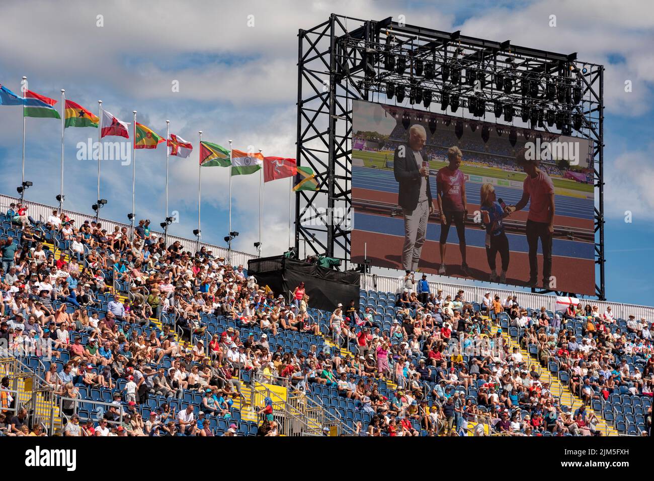 Birmingham, Großbritannien, 4.. August 2022. Zuschauer im Alexander Stadium, Birmingham, genießen die Sport Relief All-Stars Teil der Veranstaltung bei den Commonwealth Games 2022. Auf der Leinwand werden Dame Kelly Holmes und Ellie Simmonds OBE von Radzi Chinyanganya und Iwan Thomas während des Sport Relief-Events nach dem wichtigsten Althletik-Event interviewt. Flaggen der Commonwealth-Staaten fliegen über das Stadion. Quelle: Martin Anderson/Alamy Live News Stockfoto