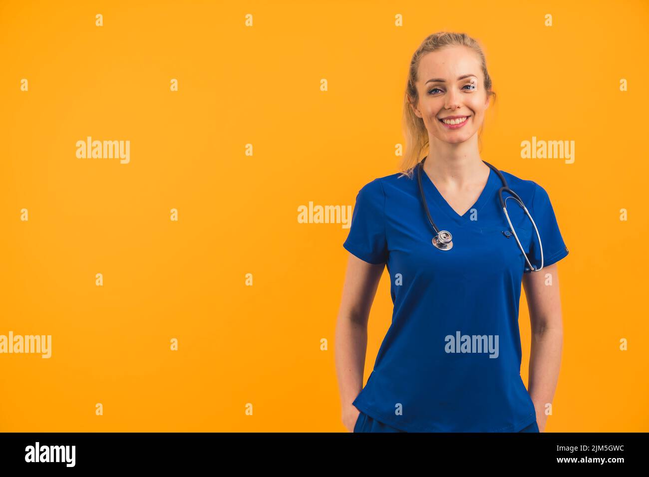 Kaukasische weibliche blonde Krankenschwester trägt Scrubs stehen selbstbewusst Hände in den Taschen Blick in die Kamera lächeln einladend. Studioaufnahme. . Hochwertige Fotos Stockfoto