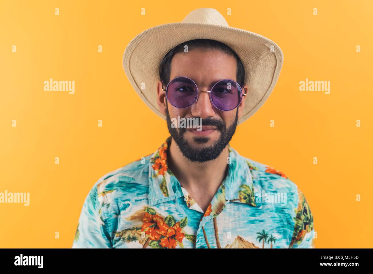 Hispanischer Mann mit Bart, Sonnenbrille mit Strohhut und gemustertem Kurzarmhemd und Blick in die Kamera. Touristen. Studioaufnahme. Hochwertige Fotos Stockfoto