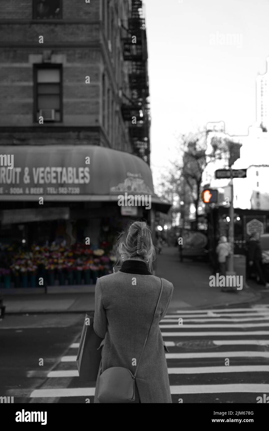 Eine vertikale Graustufenaufnahme der Frau, die gegen den Fußgängerübergang steht. Hell's Kitchen, New York. Stockfoto