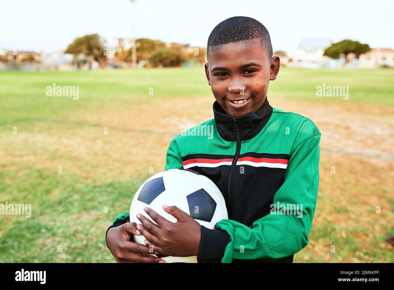 Sport zu treiben kann das Selbstvertrauen von Kindern stark verbessern. Porträt eines Jungen, der auf einem Sportplatz Fußball spielt. Stockfoto